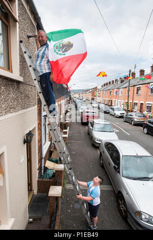 Sandy Turley inviare la bandiera messicana la sua casa a Iris nella parte occidentale di Belfast con l aiuto di suo figlio Aaron Turley come lui e altri residenti hanno ottenuto in Coppa del Mondo febbre a creare un gioco a premi e raccogliere fondi per una festa di strada il giorno della finale della Coppa del mondo. Foto Stock