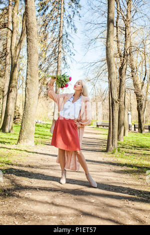 Donna Gorgeous con fiori, ritratto all'aperto. Modello femminile in rosa impermeabile e stivaletti, street fashion Foto Stock