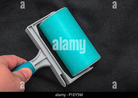 Utilizzando lo sticky pelucchi rullo su un tessuto nero per rimuovere polvere, pelliccia, capelli della camicia. Pulizia di un tessuto con un blu lavabile rullo appiccicoso. Foto Stock