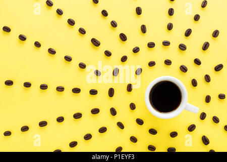 Tazza di caffè con i raggi del sole fatto di chicchi di caffè su sfondo giallo. Appartamento laico, design creativo. Sunny buongiorno & caffè nero concetto. Foto Stock