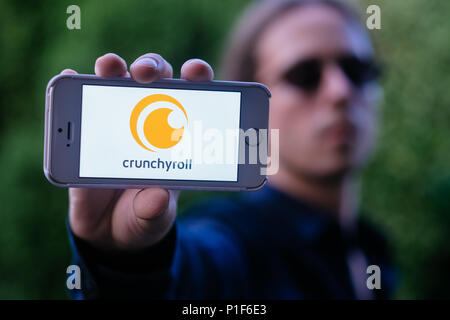 Primo piano della giovane serio tenendo iPhone bianco con logo CRUNCHYROLL sullo schermo Foto Stock