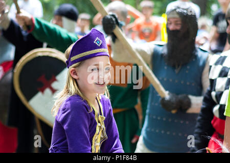 Nis, Serbia - Giugno 10, 2018: Medievale piccola principessa in abito viola e cavalieri con arma in aria in sfondo sfocato. Medioevo festival Foto Stock