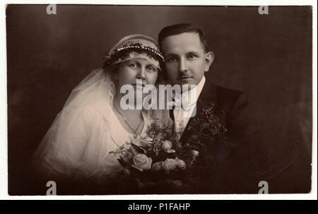 LIBEREC (REICHENBERG), REPUBBLICA CECOSLOVACCA - CIRCA 1920s: Foto d'epoca degli sposi novelli con bouquet di nozze. Sposa indossa il velo di nozze headdress. Lo sposo indossa abiti eleganti, bow-tie bianco. Vecchia foto in bianco e nero. Antico ritratto studio. 1920s. Foto Stock