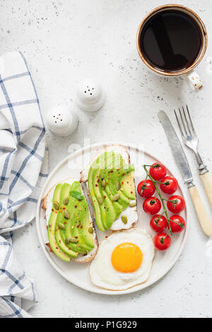 Toast con avocado, Uovo fritto, pomodori e tazza di caffè nero americano sul calcestruzzo luminoso dello sfondo. Vista superiore e copiare lo spazio per testo Foto Stock