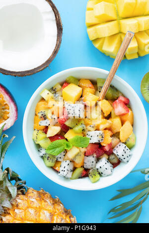 Una sana insalata di frutta con mango e ananas, pesca e pitaya luminoso su sfondo blu. Vista dall'alto. Una insalata di frutta tropicale. Cibo tailandese Foto Stock