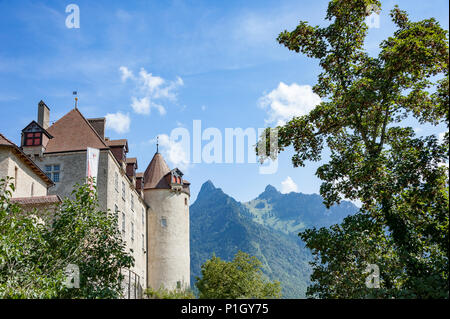 Vista attraverso gli alberi di Gruyeres Castello (Chateau de Gruyeres), contrafforti alpini della Svizzera. Estate scena, verdi alberi, cielo blu e montagne Foto Stock