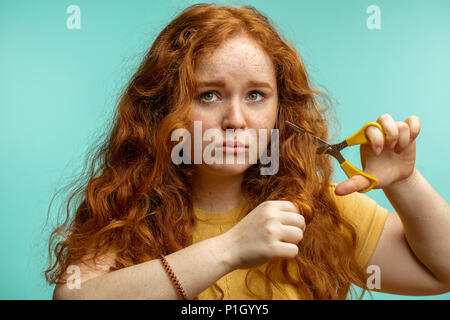 Sconvolto e la donna con il suo secco danneggiati capelli viso espressione sfondo blu Foto Stock