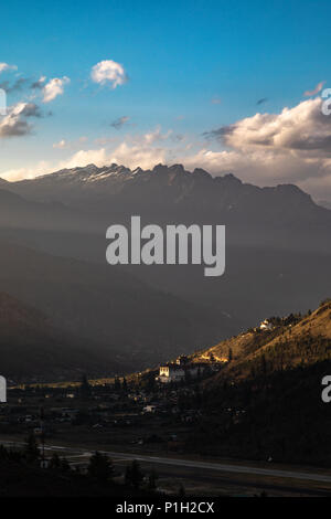 Paro Dzong riceve l'ultima luce del giorno al tramonto in uno sfondo di montagne Foto Stock