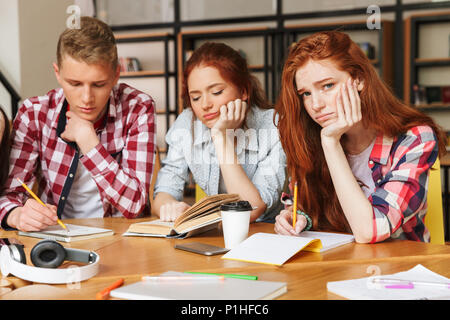 Gruppo di adolescenti stanchi di fare i compiti di scuola mentre è seduto presso la biblioteca con libri Foto Stock