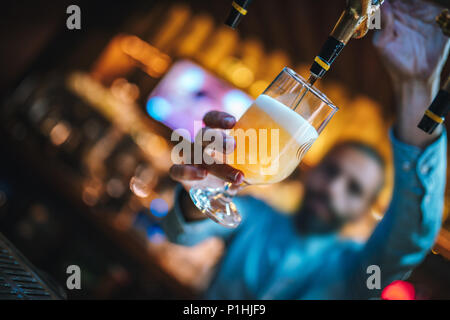 Barman o birraio di riempimento in vetro con la birra. Barman è versando birra chiara a bicchiere da birra rubinetti. Bar o night club interno. Foto Stock