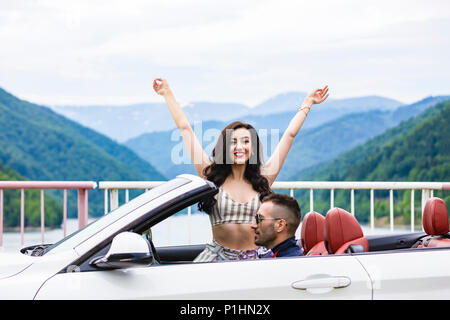 Matura in convertibile. Felice coppia giovane godendo di viaggio nel loro convertibile donna mentre i bracci di sollevamento e sorridente Foto Stock