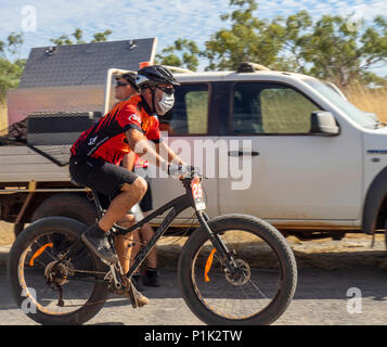 Gibb Challenge 2018 un maschio ciclista in jersey e bib a cavallo di un fatbike passando veicolo di supporto su strada sterrata Gibb River Road WA Kimberley Australia. Foto Stock