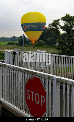 Un grande giallo mongolfiera atterra in un agricoltore il campo sul lato opposto del Leeds e Liverpool canal al di là della Crabtree Lane ponte girevole. Foto Stock