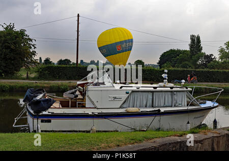 Un grande giallo mongolfiera atterra in un agricoltore il campo sul lato opposto del Leeds e Liverpool canal al di là di un incrociatore ormeggiato in barca Foto Stock