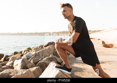 Ritratto di un bel sportivo facendo esercizi di stretching al mare al mattino Foto Stock