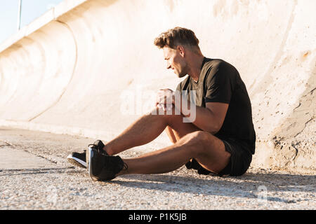 Ritratto di un ferito uno sportivo che soffrono di dolore al ginocchio mentre seduti all'aperto Foto Stock