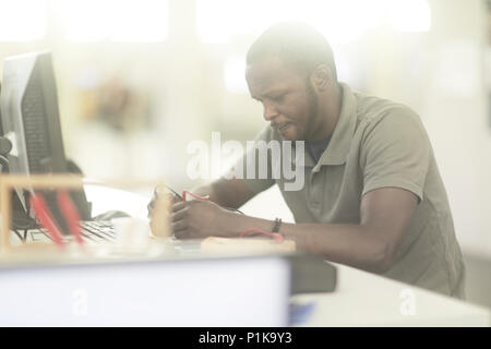 Uomo seduto alla scrivania che controlla un dispositivo con misuratori di flusso Foto Stock