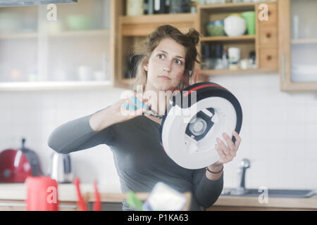 Donna in piedi in cucina che fissa un manipolatore robotico aspirapolvere Foto Stock