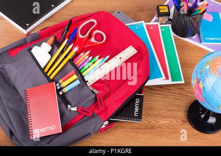Zaino con un vasto assortimento di forniture scolastiche sul desktop di un ritorno al concetto di scuola Foto Stock