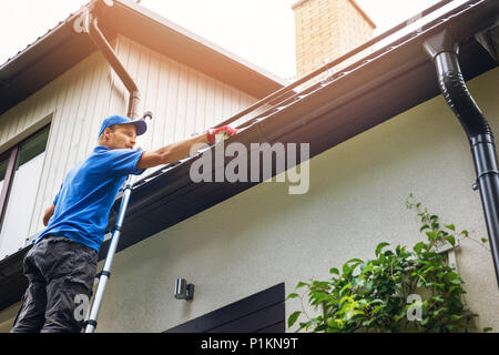 L uomo sulla scala di pulizia grondaia della casa di foglie e sporcizia Foto Stock