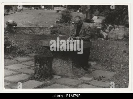 La REPUBBLICA SOCIALISTA CECOSLOVACCA - circa settanta: Retro mostra fotografica di uomo si siede al tavolo di pietra al di fuori. Bianco & Nero fotografia vintage. Foto Stock