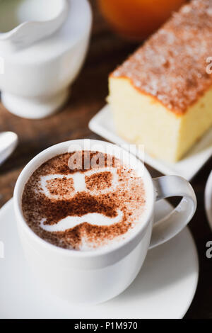 Una tazza di cappuccino con la silhouette di un paio di occhiali e un baffi formando il volto di un uomo disegnata con il cacao in polvere sulla sua schiuma, su un ta Foto Stock