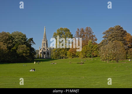 Persone relax su un prato con alberi e il Monumento a Re Leopoldo I in stile neo-gotico nel parco di Laeken a Bruxelles in un pigro e soleggiata domenica dopo Foto Stock