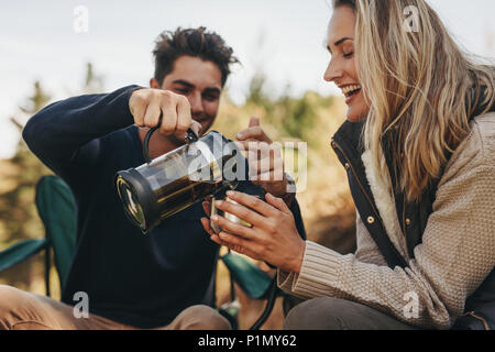 Coppia giovane avente un caffè a un campeggio. Uomo che serve caffè alla donna. Foto Stock