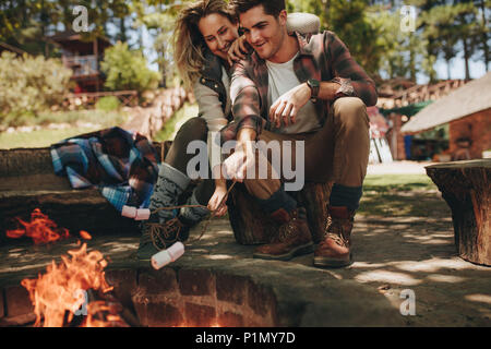 Accoppiare la tostatura marshmallows sui falò al campeggio. Uomo e donna con dolci arrosto su camping. Foto Stock