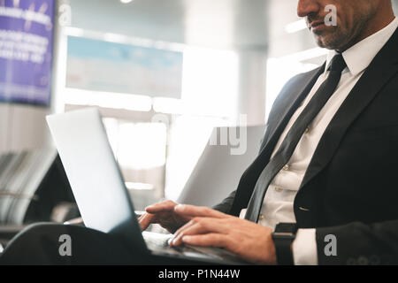 Immagine ritagliata di imprenditore vestito in tuta utilizzando computer portatile mentre è seduto all'aeroporto lobby Foto Stock