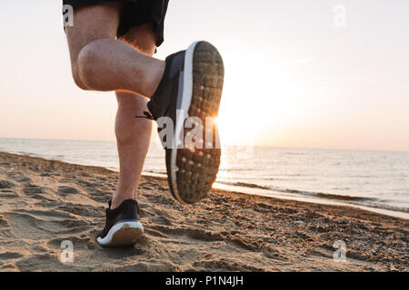 Vista posteriore di una sportivi per le gambe in esecuzione su una spiaggia di sabbia durante il tramonto Foto Stock