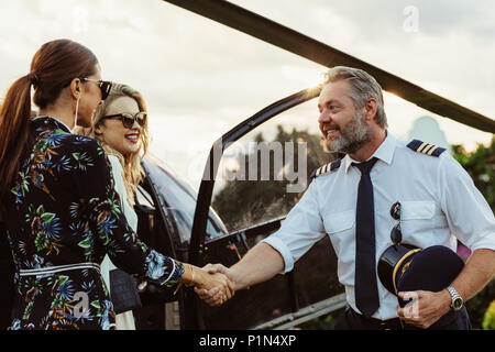 Pilota di elicottero stringono le mani con due donne e sorridente. Due donne che viaggiano da un elicottero privato con pilota li saluto. Foto Stock