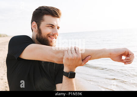 Bel giovane sportivo facendo esercizi di stretching in spiaggia durante il sunrise Foto Stock