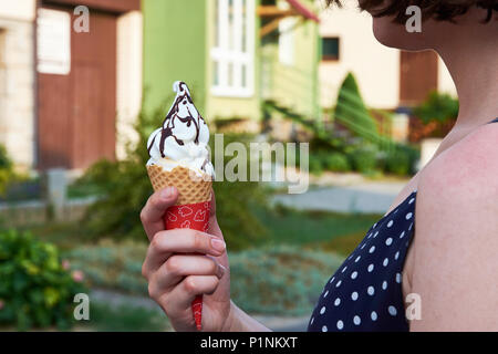 Giovane donna tenendo il gelato in mani, con case, città e alberi sfocati in background Foto Stock