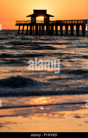 Naples, Florida giallo e arancione tramonto vista verticale nel golfo del Messico con il sole che tramonta all'interno di Molo Jetty di legno, Horizon e blu scuro oceano onde Foto Stock