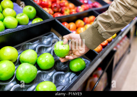 Verde mela assortiti sul ripiano espositivo in drogheria scatole in corridoio, supermercato interno, uomo persona cliente di toccare con mano che tiene la granny smit Foto Stock
