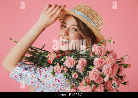 Close up ritratto di un bel giovane donna in abiti estivi e cappello di paglia tenendo i garofani bouquet isolate su sfondo rosa Foto Stock