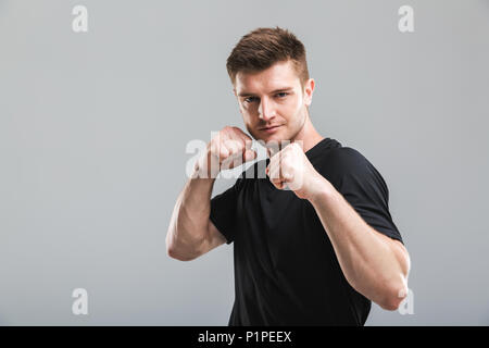 Ritratto di un giovane focalizzato sportivo in piedi pronti a combattere isolate su uno sfondo grigio Foto Stock