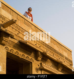 Un turista femminile guarda giù da un tetto in il villaggio abbandonato di Kuldhara nel distretto di Jaisalmer, avente una reputazione di essere ossessionato Foto Stock