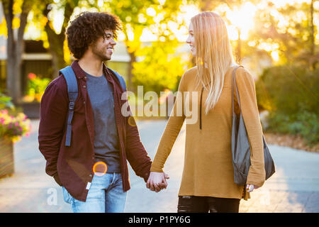 Ragazzo e ragazza camminare, parlare e tenendo le mani sul campus universitario al tramonto; Edmonton, Alberta, Canada Foto Stock