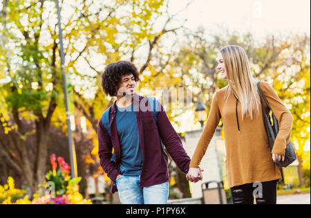 Ragazzo e ragazza camminare, parlare e tenendo le mani sul campus universitario al tramonto; Edmonton, Alberta, Canada Foto Stock