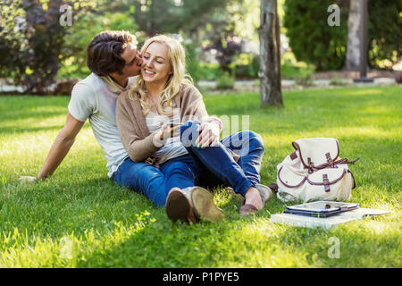 Una giovane coppia condivide un momento romantico insieme seduta sul prato del campus universitario; Edmonton, Alberta, Canada Foto Stock