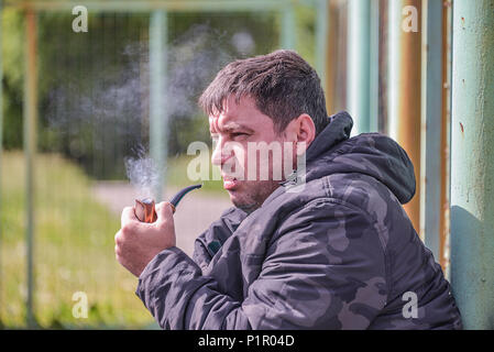 L'uomo sta fumando una tubazione, close-up, nel raffreddare ventoso, il fumo è volare in aria Foto Stock