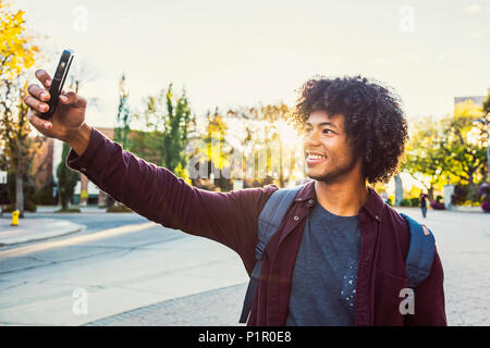 Un giovane maschio americano africano studente universitario pone per un autoritratto con il suo smart phone; Edmonton, Alberta, Canada Foto Stock