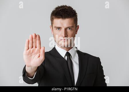 Ritratto di un giovane serio imprenditore della tuta che mostra il gesto di arresto con il palmo della mano isolate su uno sfondo grigio Foto Stock