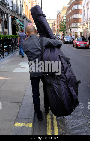 Uomo che porta double bass su strada, Soho, London, England, Regno Unito Foto Stock