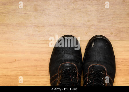 Una coppia di sporco utilizzato in acciaio con puntale stivali da lavoro isolato su un laminato pavimento in legno Foto Stock