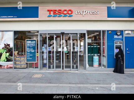 Vista esterna di un supermercato Tesco express con donna musulmana withdrwing denaro dal bancomat. Negozi e people shopping a Harrow, Middlesex, London, Regno Unito Foto Stock