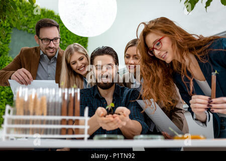 Università collega biologi tenendo un giovane pianta nel suolo in mani e controllare la qualità del campione. Foto Stock