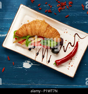 Appetitosi sandwich vegetariano con croissant e verdure giacente sulla piastra piana di forma rettangolare, ciotola di olive e pomodori ciliegia ed essiccati goji bacche sc Foto Stock